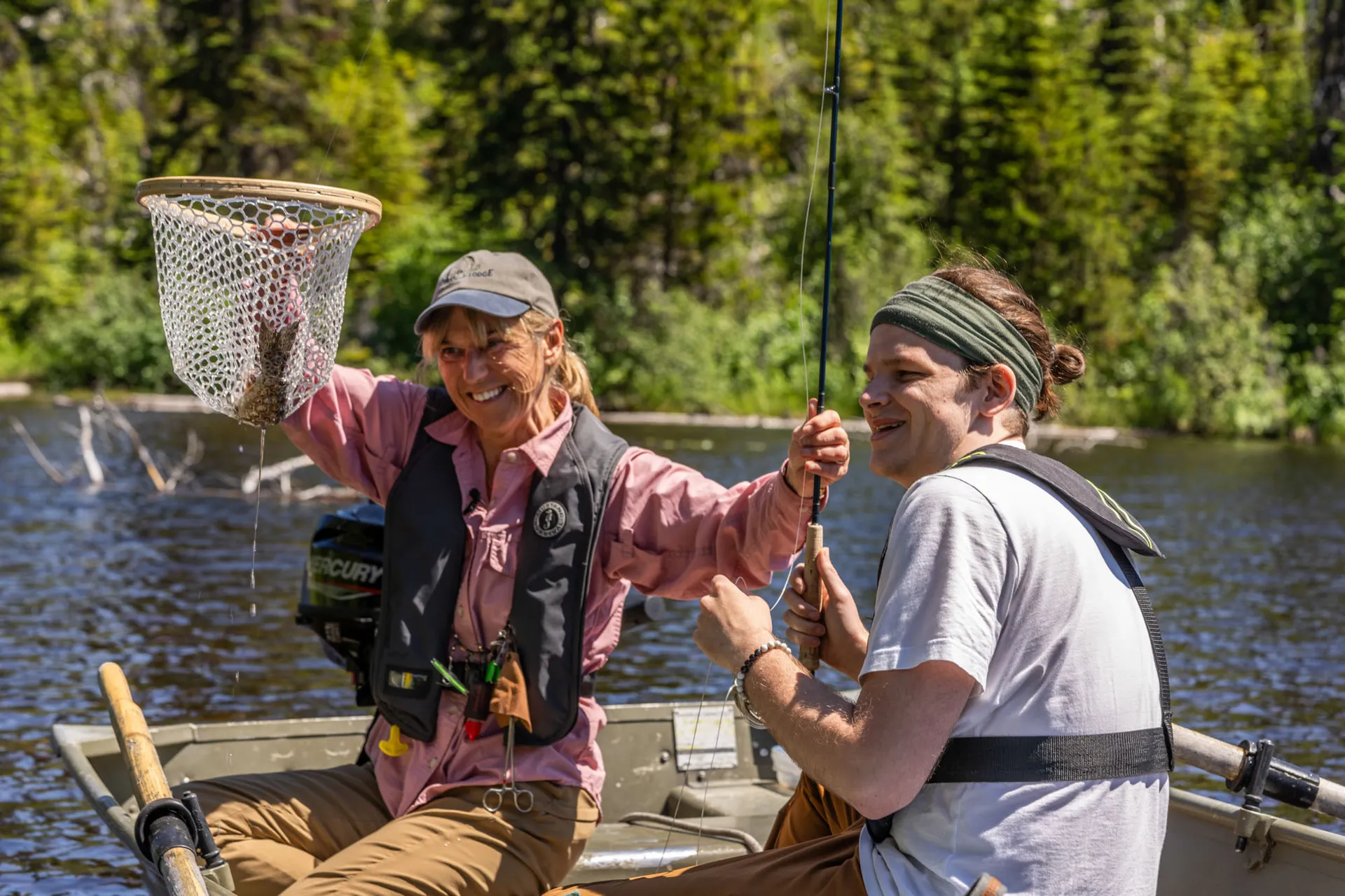 A guide lifting a netted trout beside a laughing guest in a boat