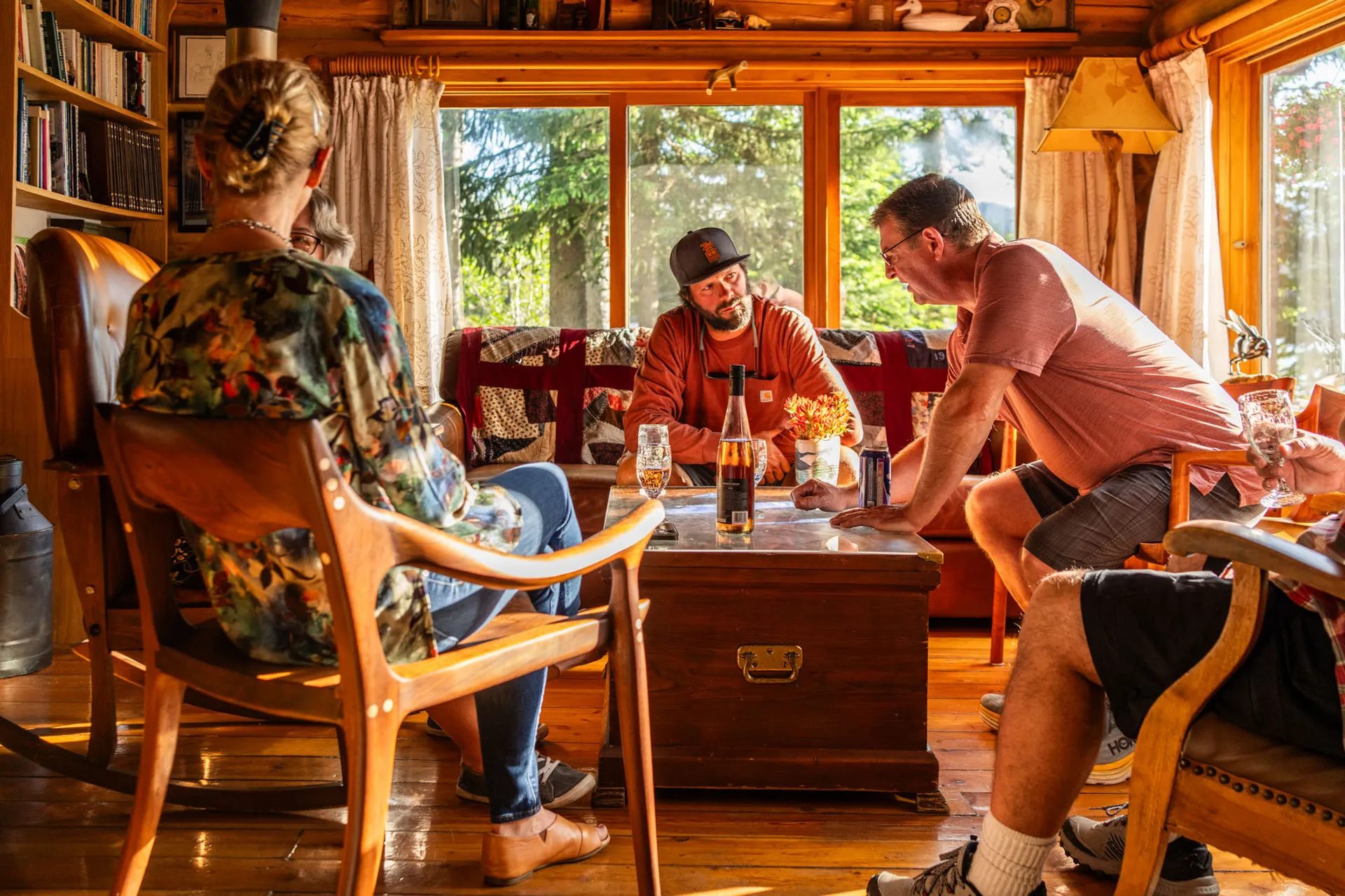 Four guests talking in the lodge's log lounge around a low wooden chest, in warm afternoon light