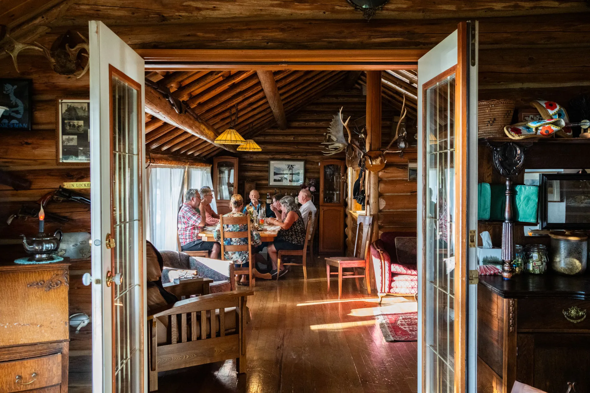 View through open French doors into the log dining room, where guests are seated at a long table