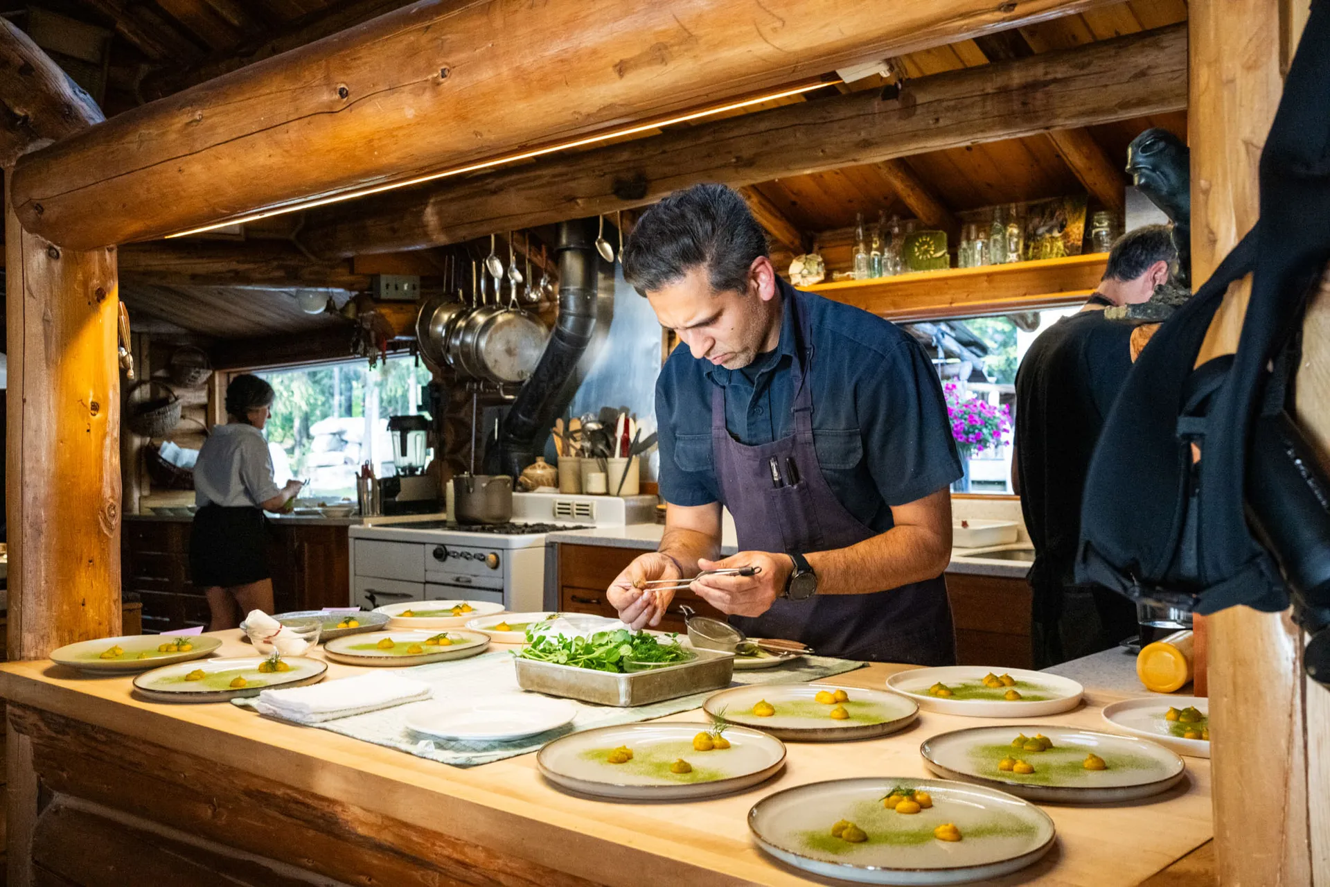Chef plating a row of dishes along the pass in the lodge's timber kitchen