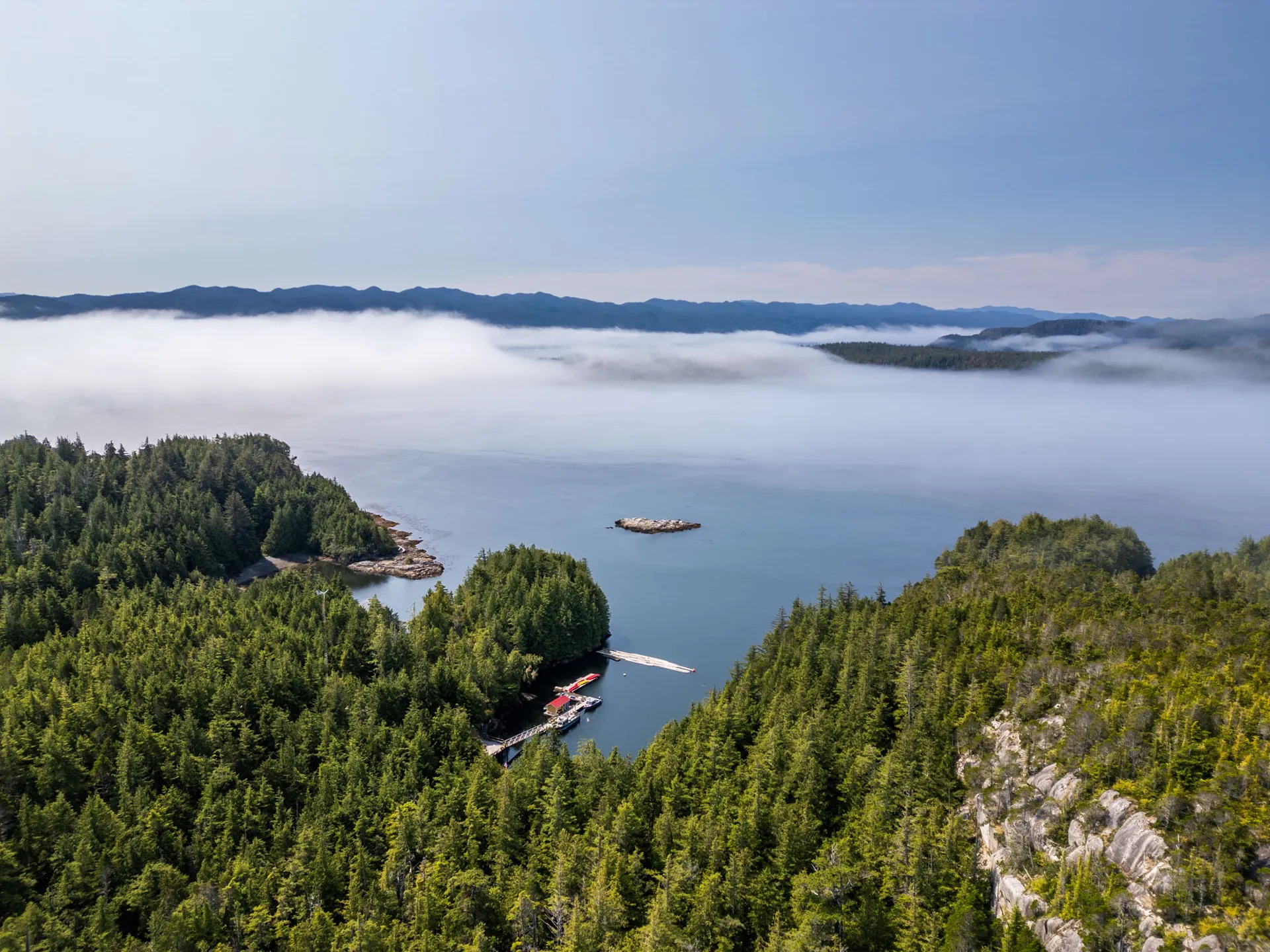 Aerial view of the resort's dock and cabins tucked into a forested cove, with fog banked over the strait beyond