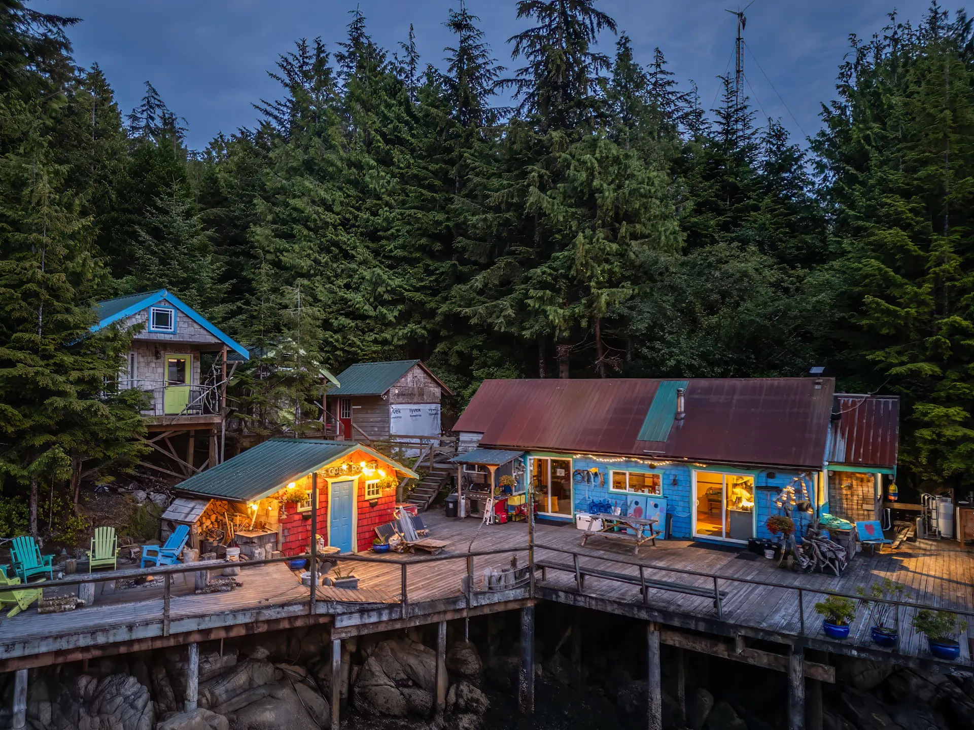 God's Pocket Resort at dusk, its red and blue timber cabins lit along a wooden boardwalk above the water