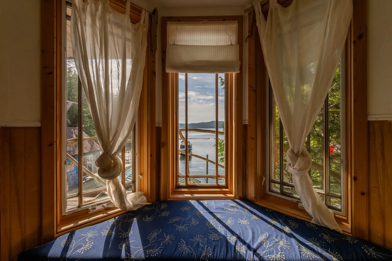 Corner guest room with wood-panelled walls and a bed set into a window bay looking out to the dock