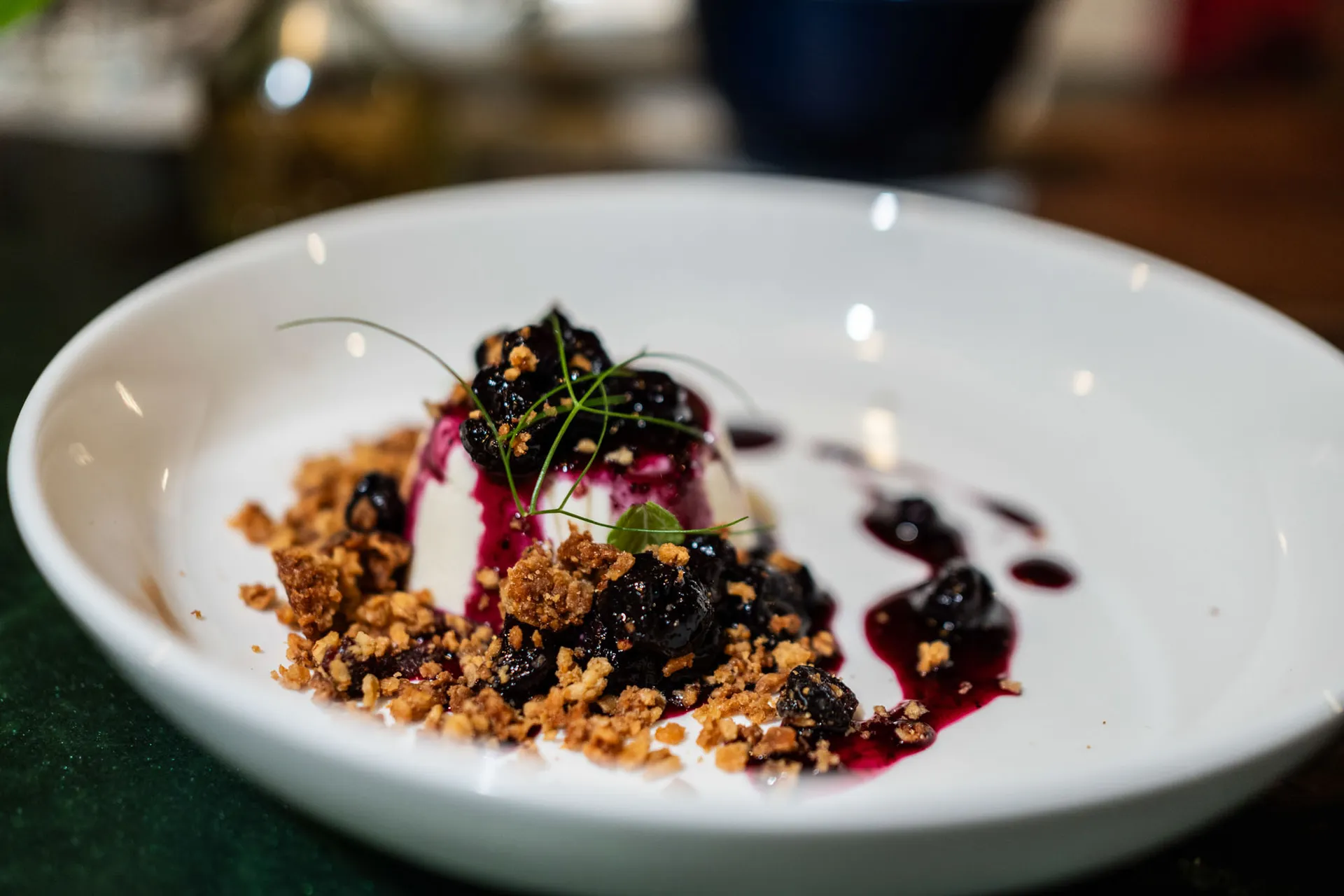 Panna cotta plated with blueberry compote and crumble in a shallow white bowl