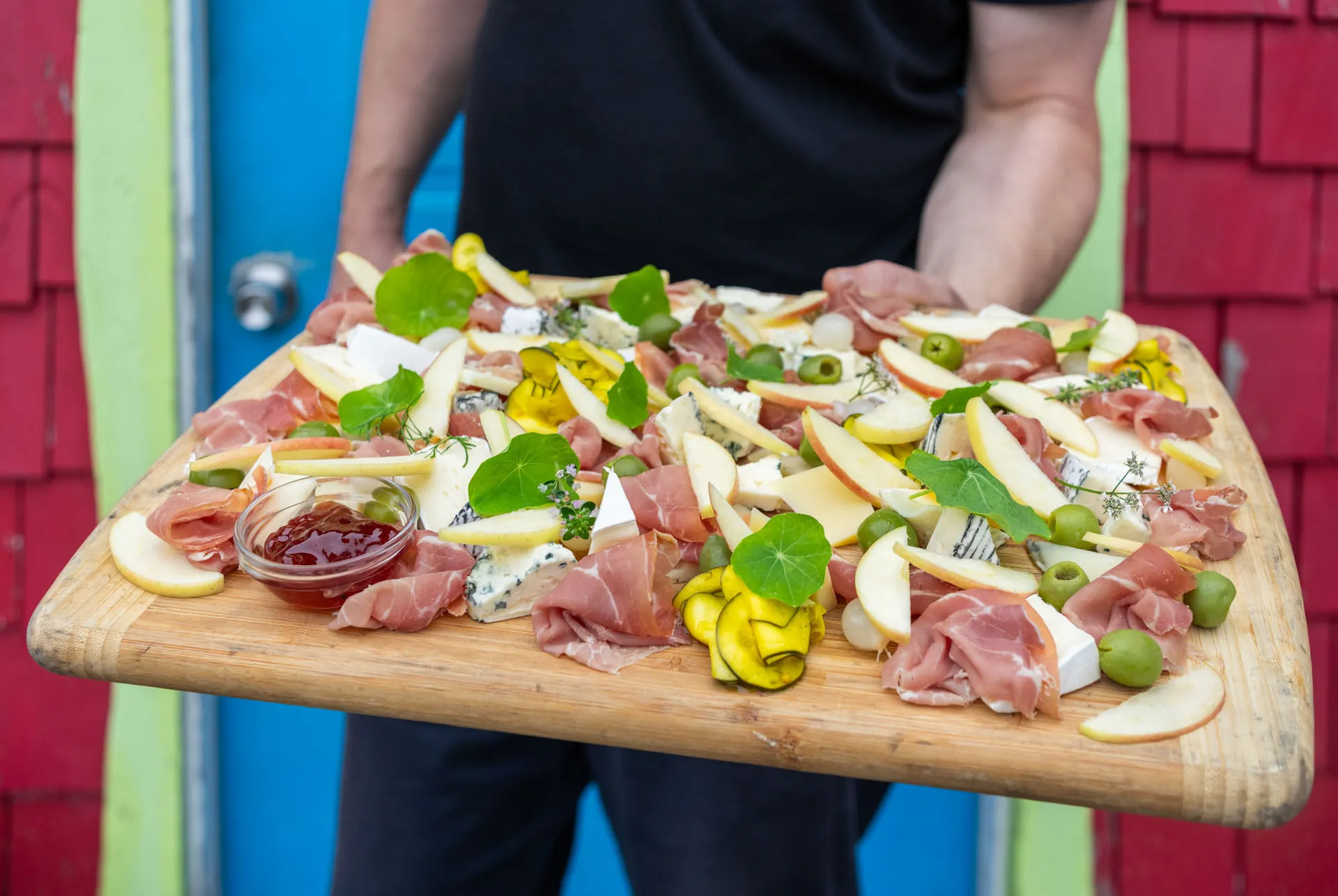 Wooden serving board loaded with prosciutto, blue cheese, apple slices, olives and nasturtium leaves