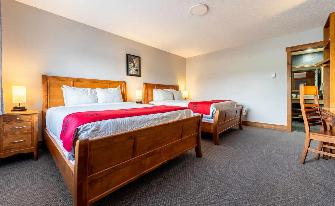 Guest room with two queen beds, wooden headboards and red blankets under soft lamplight