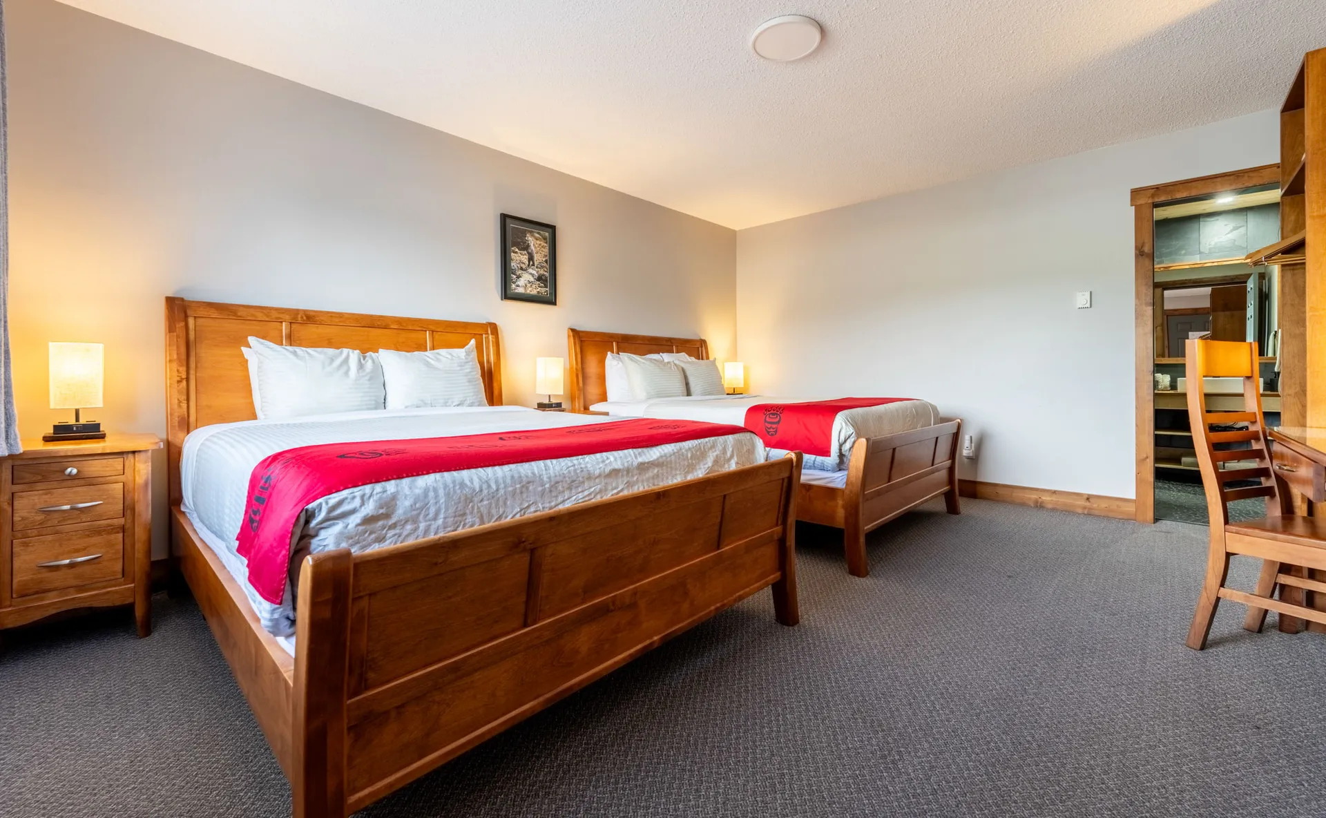 Guest room with two queen beds, wooden headboards and red blankets under soft lamplight
