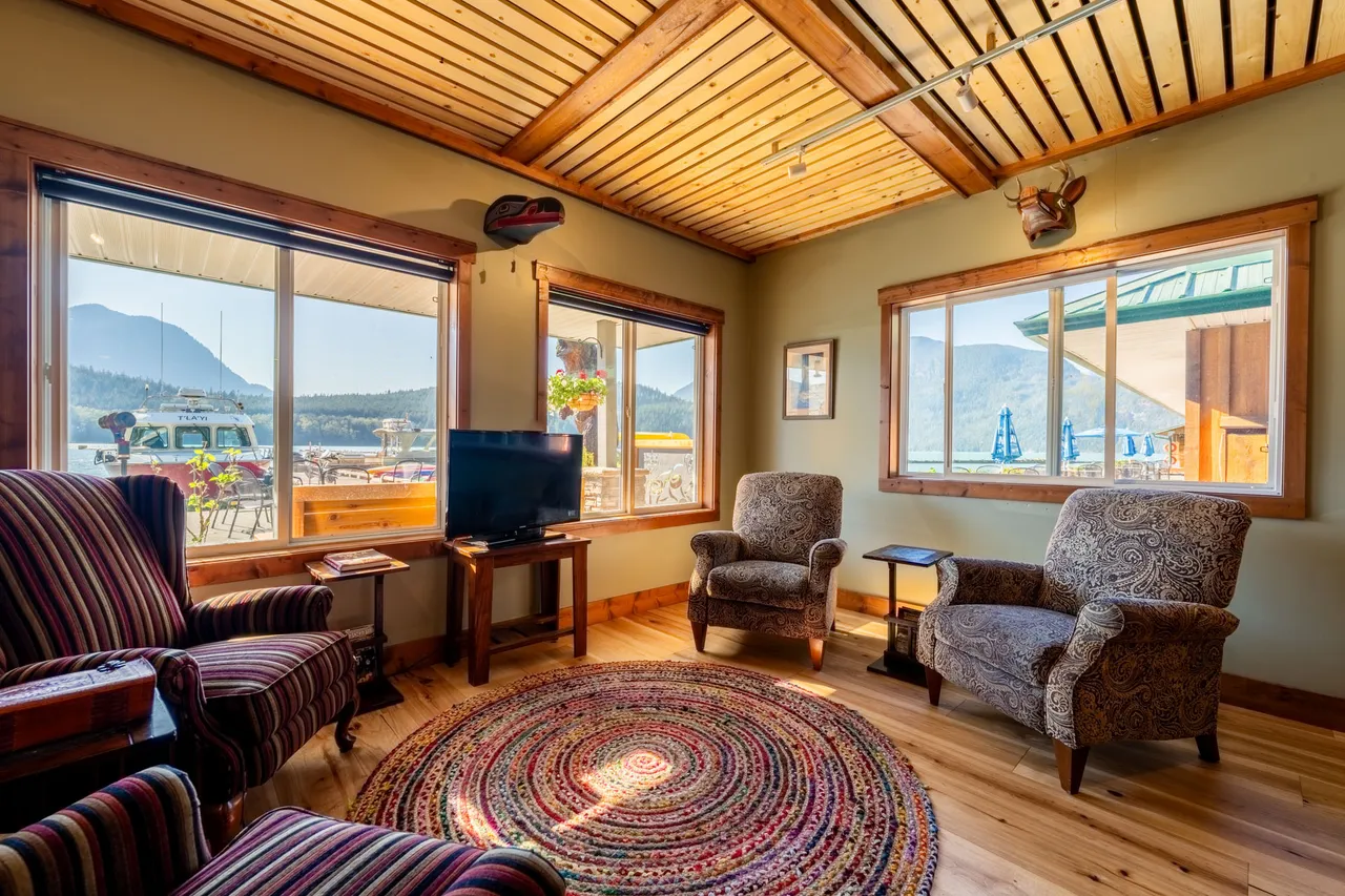 Lounge with a cedar-planked ceiling, armchairs and windows framing the inlet and the lodge's floating dock