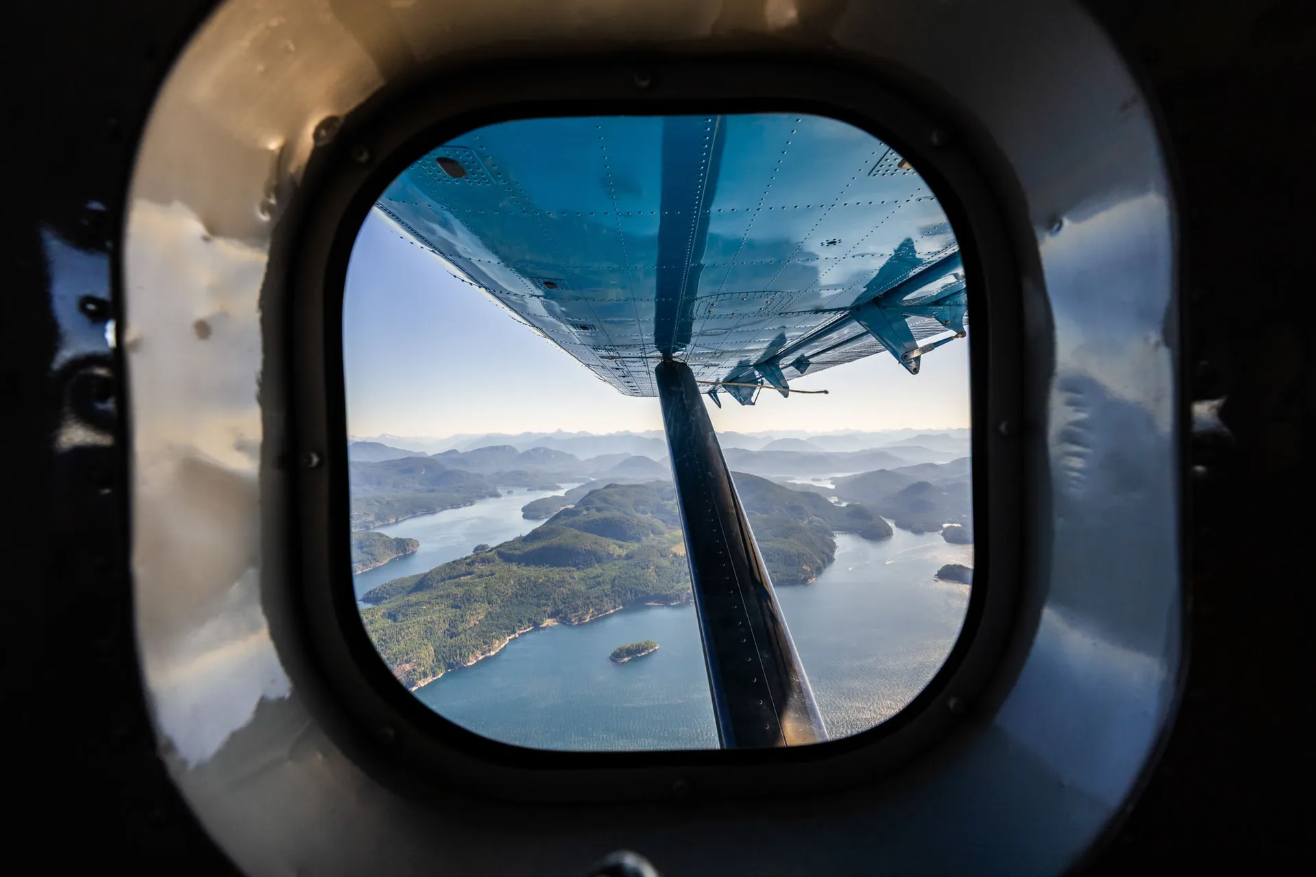 View through a floatplane window over forested islands and channels on the flight in to the lodge