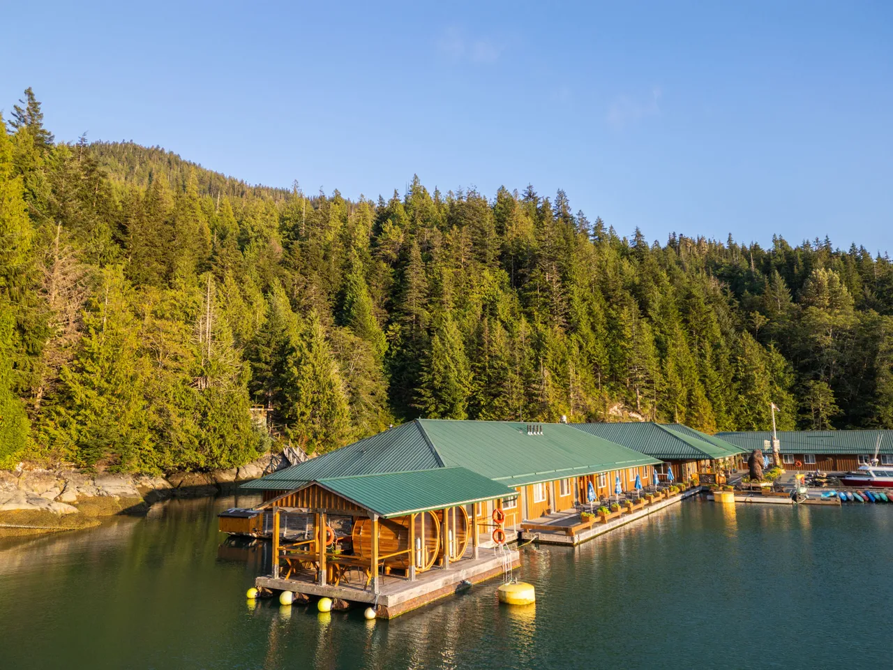 Aerial view of Knight Inlet Lodge, a green-roofed floating lodge moored against a forested shoreline in a sheltered cove