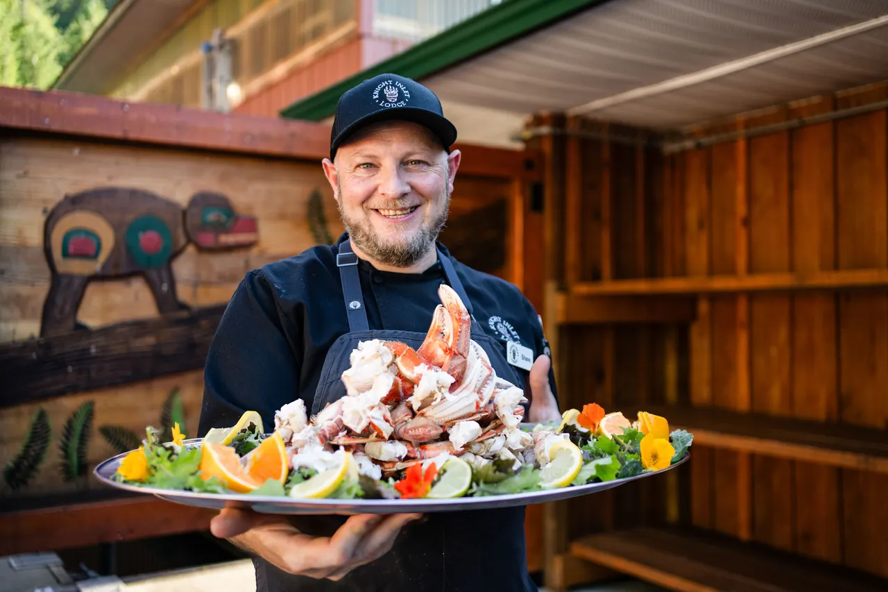 Chef holding a platter of freshly cooked Dungeness crab garnished with citrus and edible flowers outside the lodge