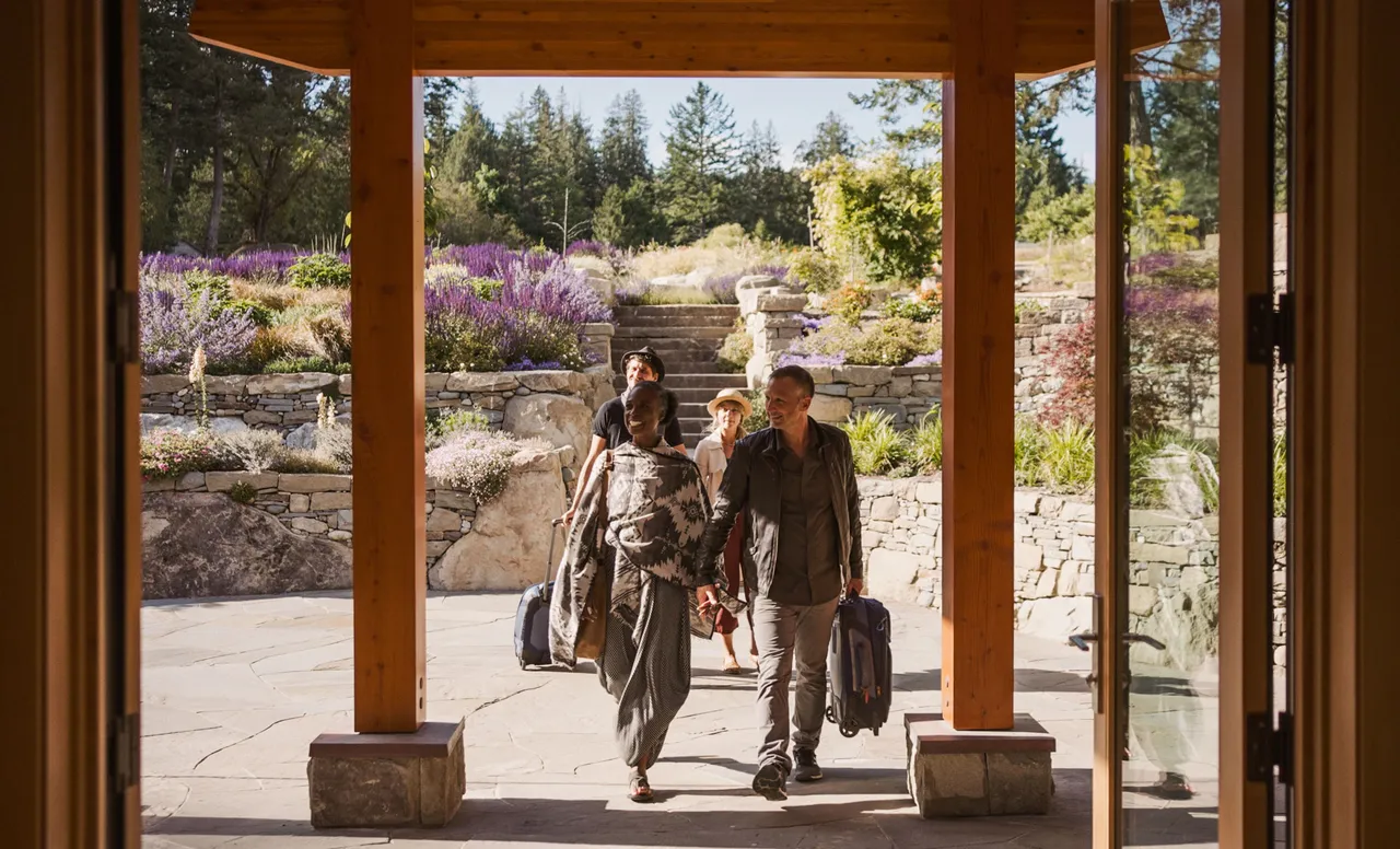 Guests arriving with luggage through the timber entrance colonnade, gardens and stone terracing behind