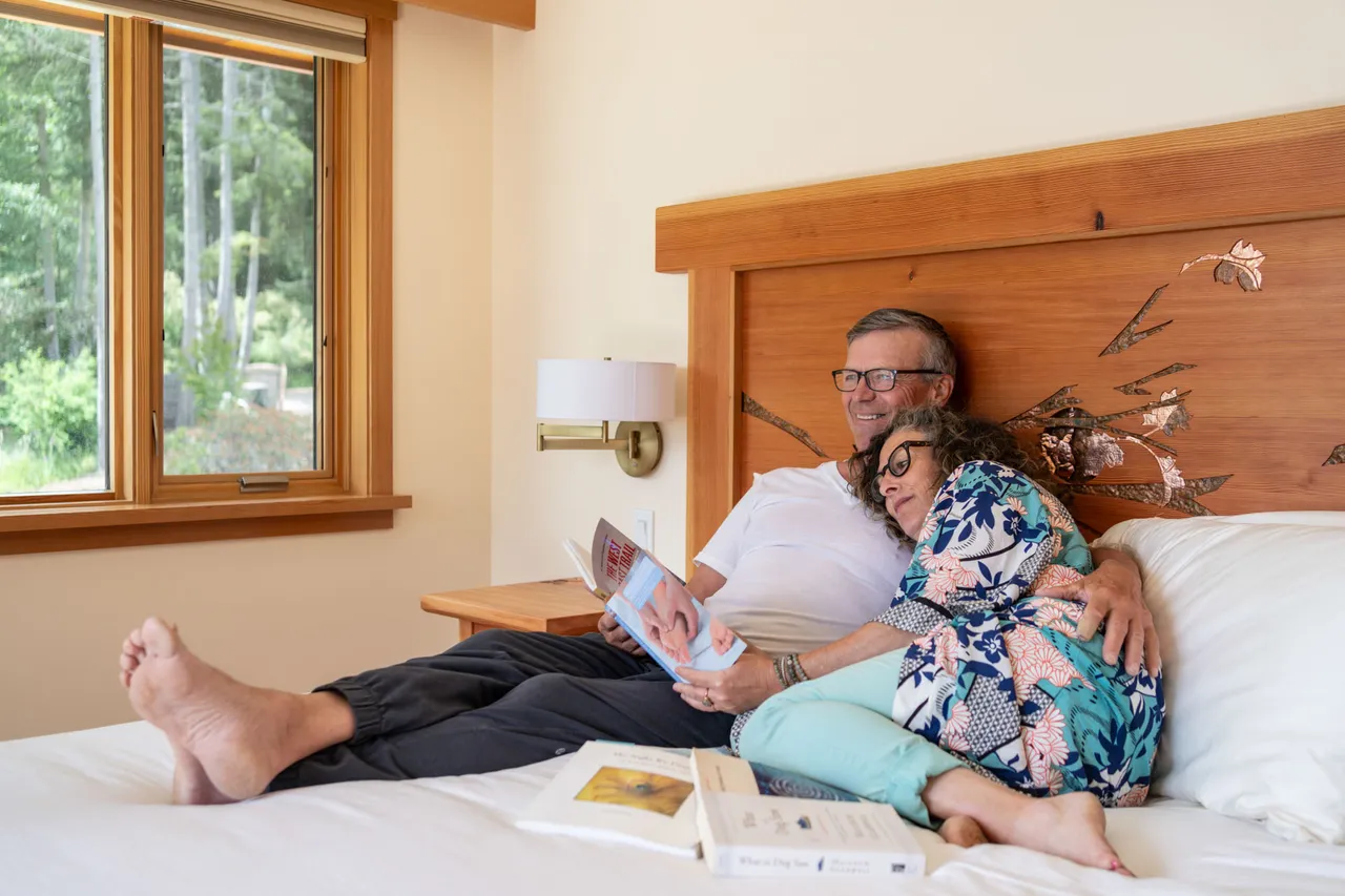 Couple reading on a king bed with a live-edge timber headboard beside a window onto the garden