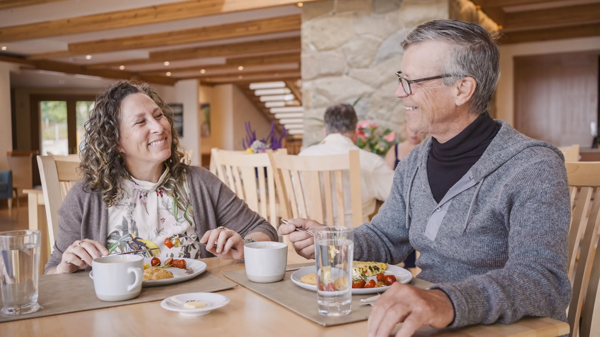 Two guests over breakfast at a wooden table in the dining room, a stone fireplace column behind them