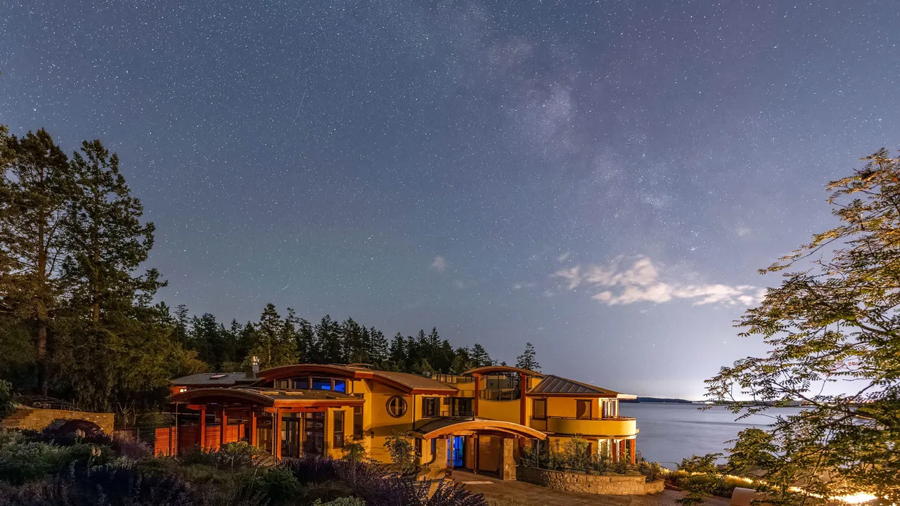 The oceanfront guesthouse glowing beneath a star-filled night sky, with the Salish Sea beyond