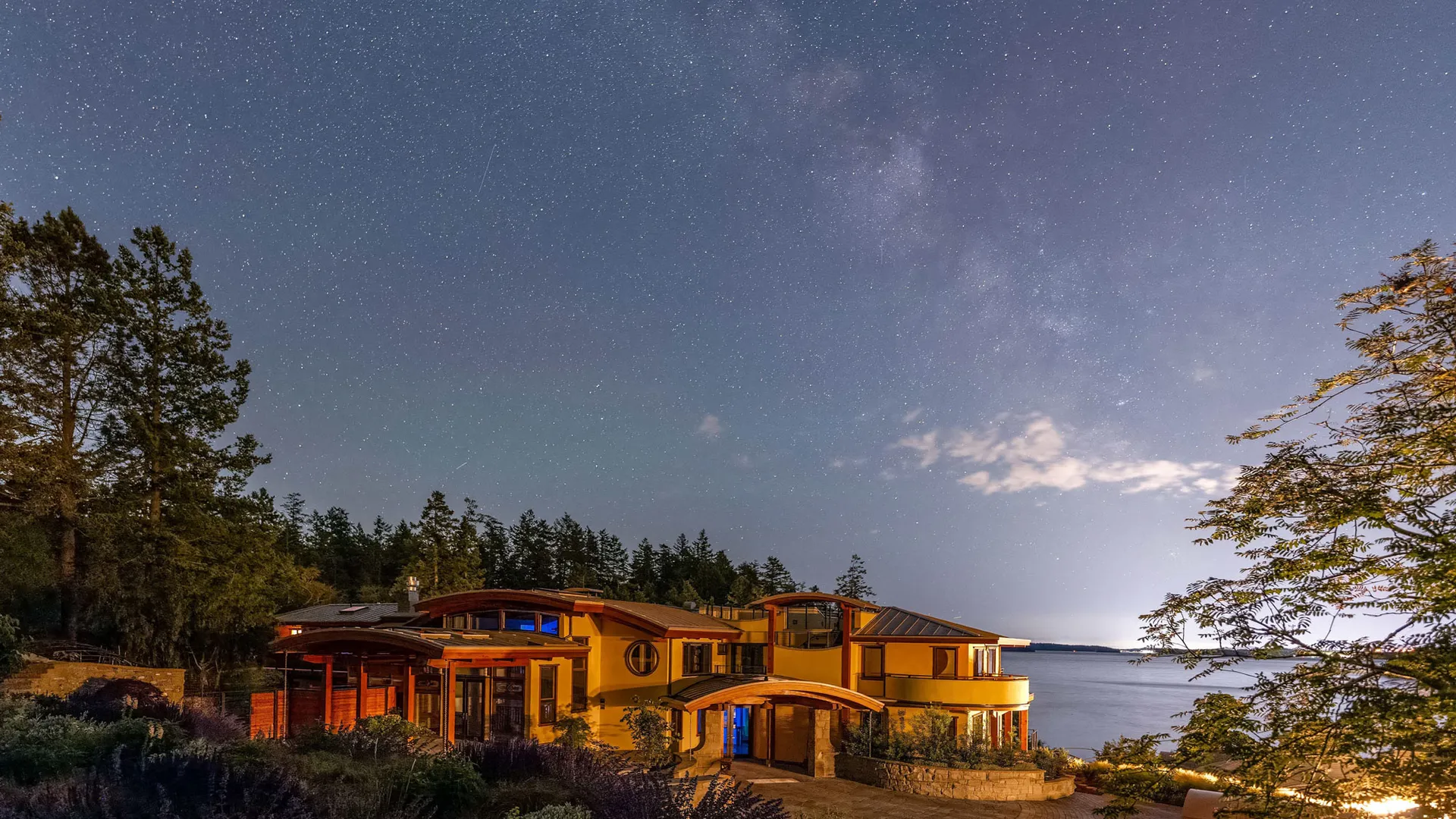 The oceanfront guesthouse glowing beneath a star-filled night sky, with the Salish Sea beyond