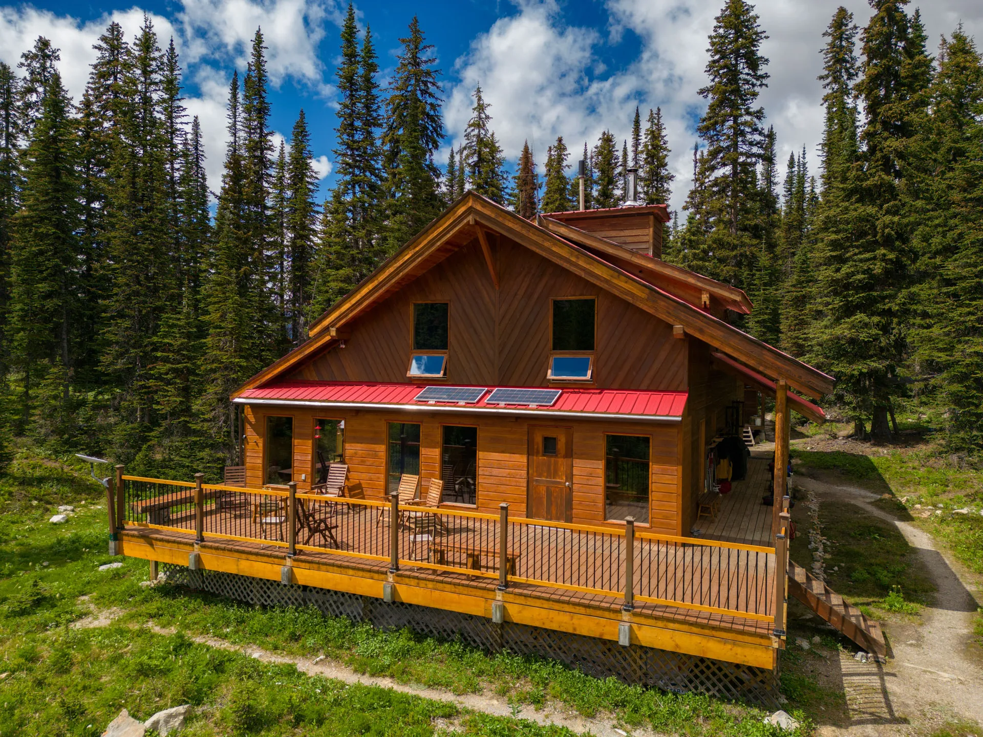Mistaya Lodge, a timber lodge with a red roof and wraparound deck, standing in alpine meadow ringed by spruce