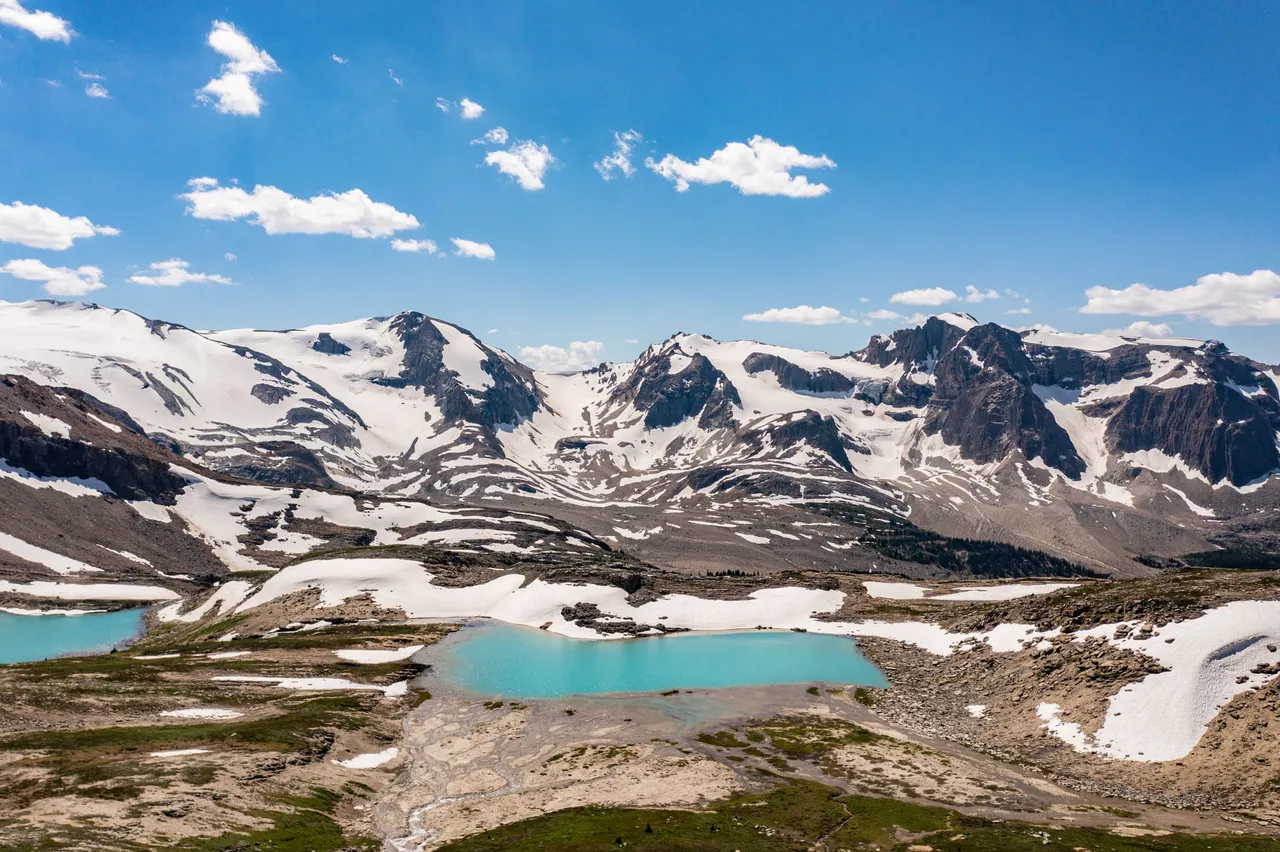 Glaciated peaks rising above two turquoise meltwater tarns and patches of late-season snow