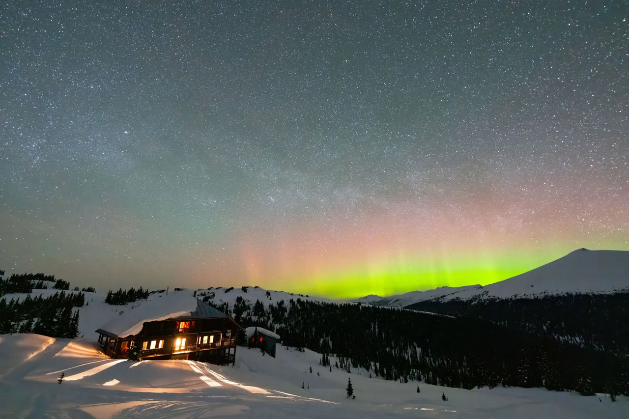 Green aurora over the snow-covered lodge and surrounding ridges at night