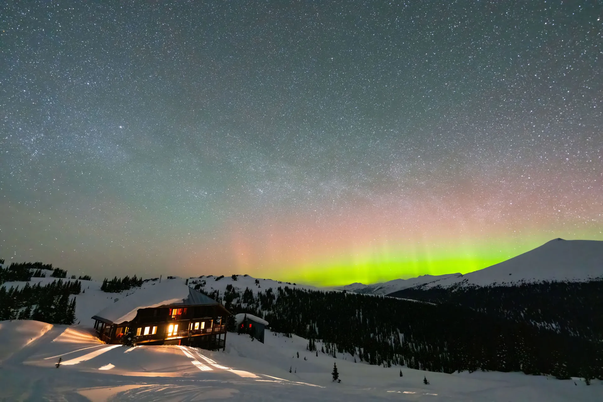 Green aurora over the snow-covered lodge and surrounding ridges at night