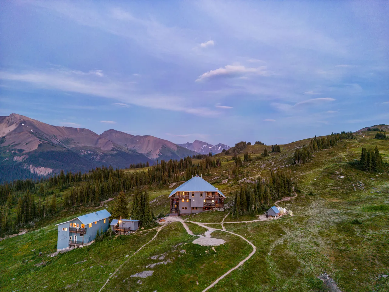 Aerial view at dusk of the lodge and its separate chalet on open meadow, ranges receding behind