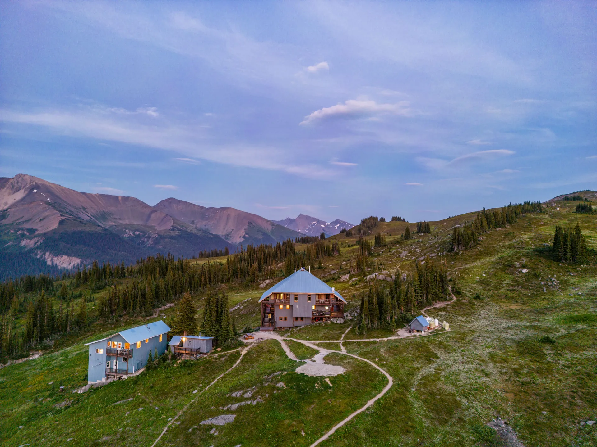 Aerial view at dusk of the lodge and its separate chalet on open meadow, ranges receding behind