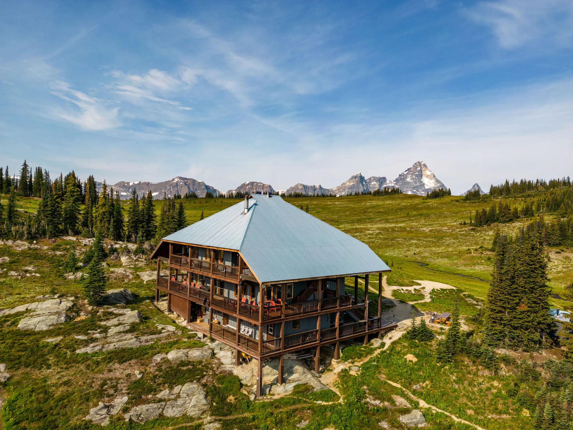 The lodge's blue roof and wraparound verandas seen from the air, sharp peaks on the horizon