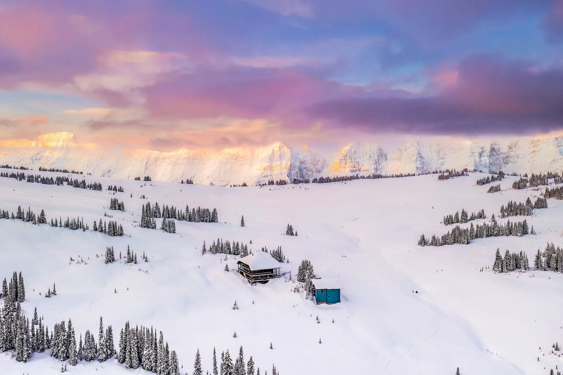 The lodge in deep winter snow below a long ridge, under pink and violet dawn cloud