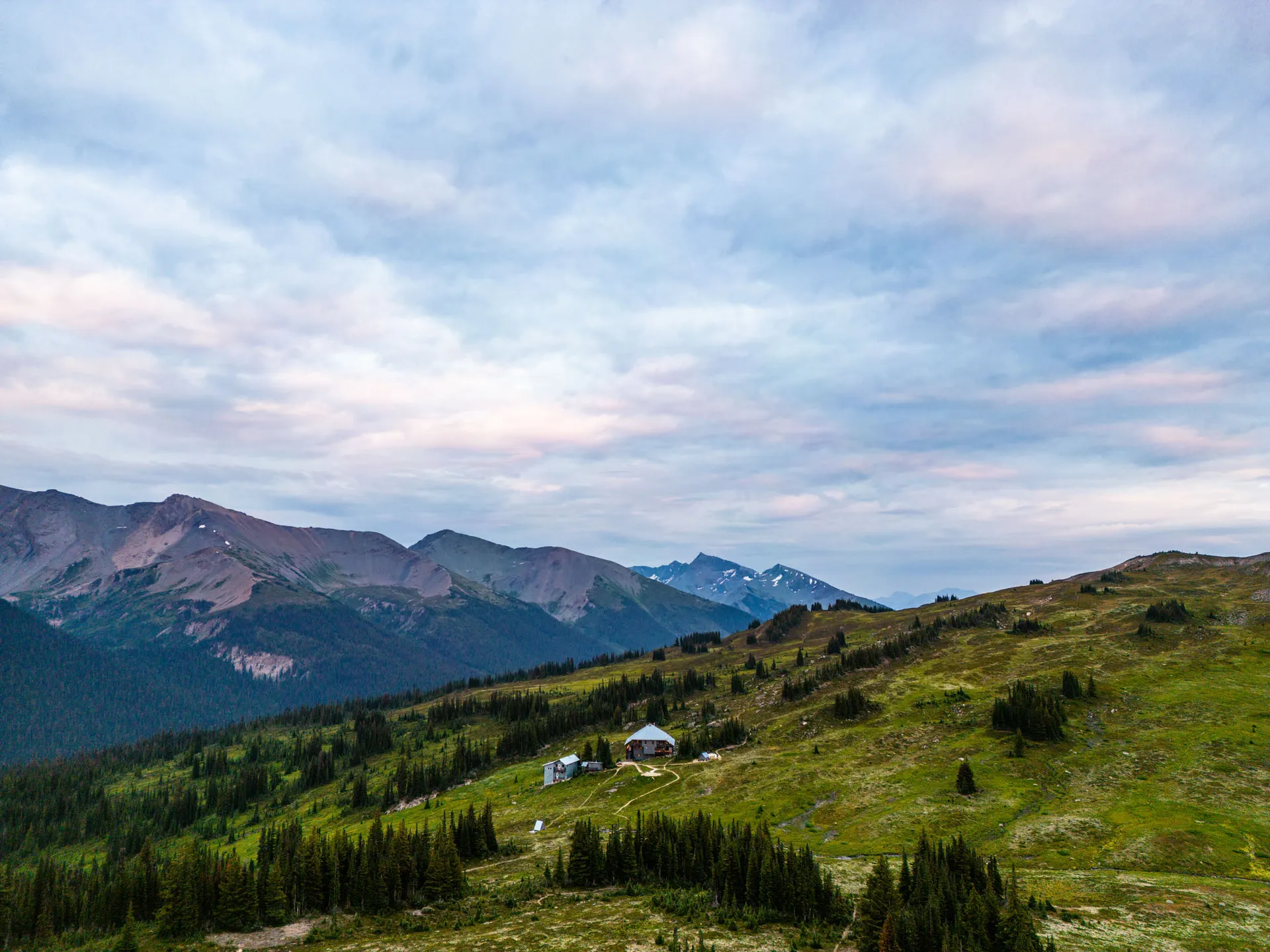 The lodge seen at a distance, standing alone in green alpine meadow above treeline with ranges beyond