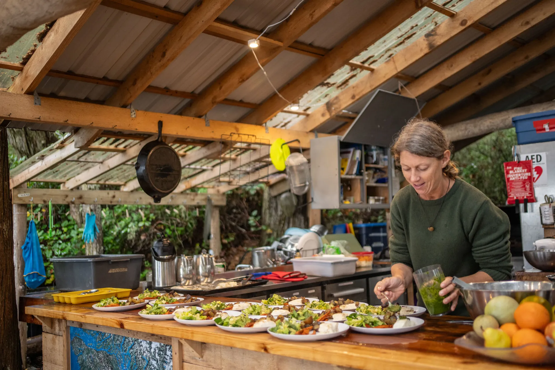 Camp cook plating a row of salads along the timber counter of the open-air kitchen shelter